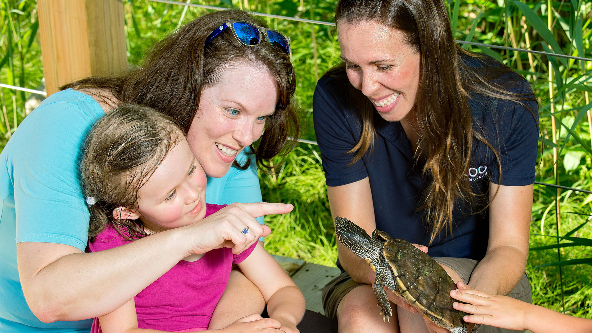 little girl with her mom at the Ecomuseum Zoo next to a zoo-keeper and a turtle